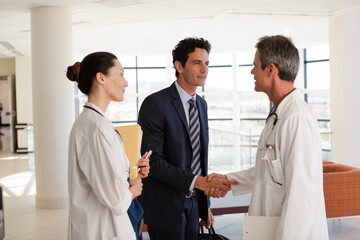 Poster - Doctor and businessman handshaking in hospital lobby