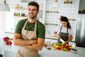 Wall Mural - Young happy couple is enjoying and preparing healthy meal in their kitchen