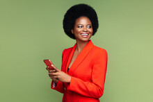 Successful African Businesswoman Hold Smartphone Look Aside With Confident Happy Smile. Afro American Young Entrepreneur Female In Luxury Red Suit With Mobile Phone Isolated Over Green Studio Wall