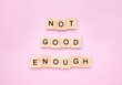 Phrase 'not good enough' on wooden blocks on pink background