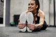Muscle stretching in spot training. A female person sits on the gym floor and stretches her leg and foot muscles. Women's hands hold the sole of the sneaker and stretch the leg muscles, worming up