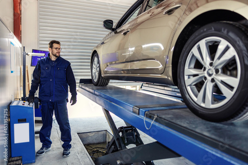 Technical inspection of the car. Car diagnostics on technical inspection. A man in a blue uniform stands next to the car and lifts it into the garage with an automatic crane by pressing a button