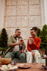 Wall Mural - Vertical portrait of two African-American young women enjoying drinks at outdoor party with fairy lights, copy space