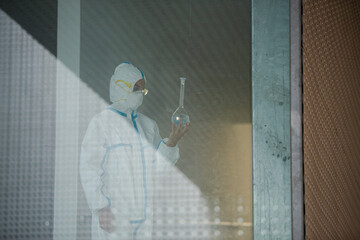 Scientist in clean suit examining liquid in test tube