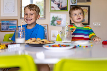 Funny male brothers eat cookies with round multi-colored sweets m&m and drink milk.