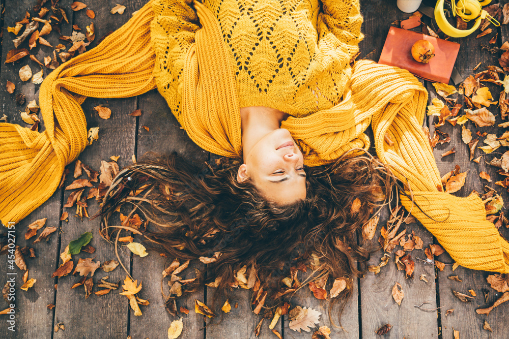 Young beautiful woman lies on autumn foliage in the park. - obrazy, fototapety, plakaty 