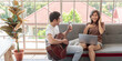 © Bangkok Click Studio - Young attractive Asian couple sitting together on a couch. Man playing guitar and woman looking at laptop wearing headphones. Concept for love and couple relationship