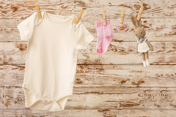 Wall Mural - Baby clothes, pacifier and toy hanging on rope against light wooden background
