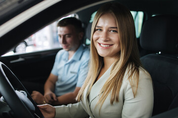 Bussines woman choosing car i car showroom. Salesperson sitting in car with customer and show desing