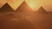 Female Traveller Looks To The Silhouette Of Pyramids At The Sunset In The Desert. Aerial Shot.