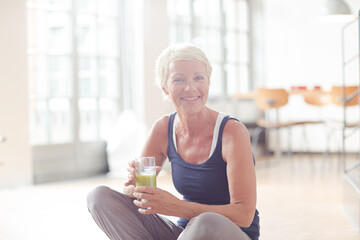 Older woman drinking juice on exercise mat