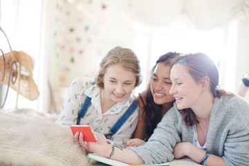 Wall Mural - Three teenage girls using smart phone together while lying on bed in bedroom