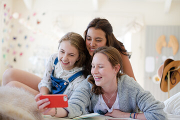 Three teenage girls using smart phone together while lying on bed