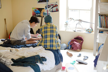 Wall Mural - Two teenage boys sitting on bed in messy room