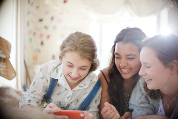 Three teenage girls using smart phone together while lying on bed