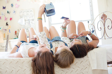 Wall Mural - Three teenage girls taking selfie while lying on bed in bedroom