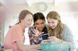 Three teenage girls looking at photograph while sitting at table