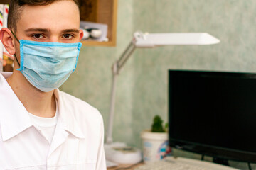 Wall Mural - a young doctor in a white coat and a protective hygienic mask in his office