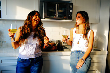 Wall Mural - Cheerful Mexican woman and mother enjoying wine in kitchen at home