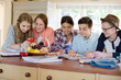 © KOTO - Group of smiling teenagers gathered around table in dining room