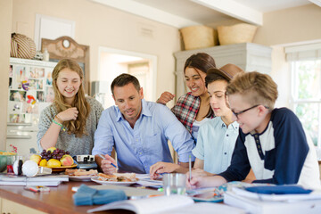 Teenagers with mid adult man sitting at table in dining room