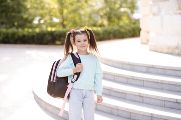 Wall Mural - Smiling sweet happy little kid girl 5-6 year old wear casual clothes and backpack. Pupil child prepare for studying. Back to school. Autumn season. Happiness. Childhood. Look at camera.