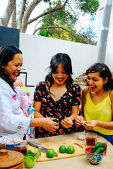 Cheerful teenager girl preparing salsa with aunt, mother and baby at kitchen counter in backyard