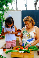 Girl peeling garlic by grandmother chopping vegetables on cutting board at kitchen counter in backyard