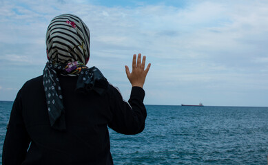 The silhouette of a sad woman or girl standing alone on the seaside and waving her hand to the distant ship with feeling lonely. Time to go. Missing someone. Desire to go far away. Time to say goodbye