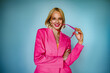 Happy smiling fashionable woman wearing trendy pink fuchsia color blazer posing on blue background. Waist up studio portrait with natural light.  Copy, empty space for text