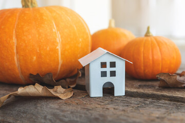 Autumnal Background. Toy house and pumpkin on wooden background. Thanksgiving banner copy space. Hygge mood, change of seasons concept. Hello Autumn with family Halloween party.