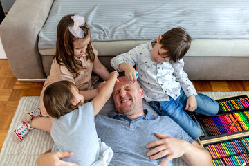 lovely family having fun together at home. photo of a one son and two daughters drawing their father