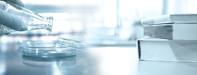 Wall Mural - scientist holding flask with petri dish and stack of book in research science lab banner background