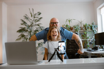 laughing daughter with funny daddy pose together shooting new video for blog at home