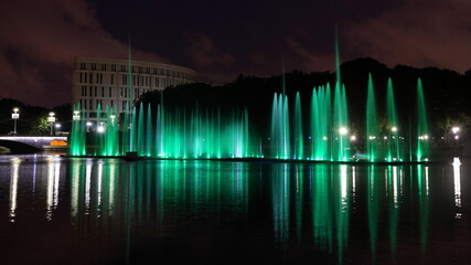 Poster - Colorful green illuminated fountains on the Svisloch River in the Yanka Kupala Park at summer night on sky background , a beautiful view of Minsk , a famous national landmark of the capital of Belarus