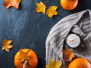 Wall Mural - A cup of coffee latte or cappuccino with pumpkin on a dark table with autumn maple leaves, a warm knitted scarf copy space