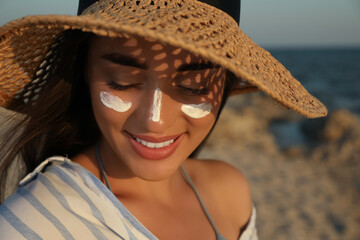 Wall Mural - Happy young woman with sun protection cream on face at beach