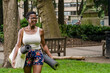 © Drew Dennis/Cultura Creative - Smiling woman with exercise mat walking in park