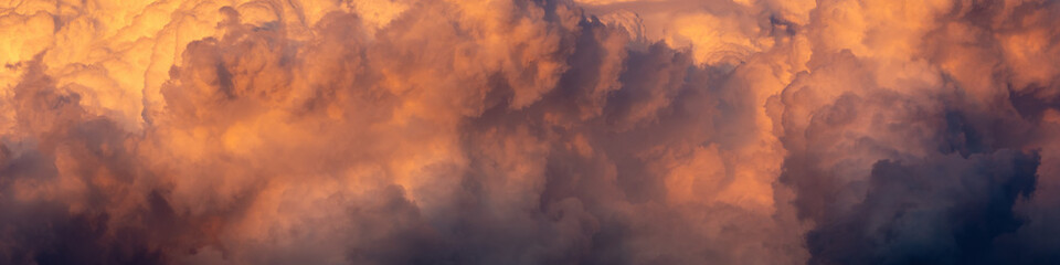 Wall Mural - a wide panoramic view of an orange-purple stormy sunset sky with cumulus clouds. atristic moody image for dramatic design or decoration