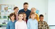 © VAKSMANV - Portrait of happy handsome young Caucasian male teacher with diverse mixed-race children pupils standing in classroom looking at camera and smiling Kids with man tutor posing in class School education