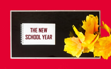the text NEW SCHOOL YEAR is written on a notepad on a black and red background with orange foliage. Back to school concept for the new school year.