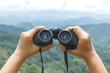 © AungMyo - Hands holding binoculars on mountains background