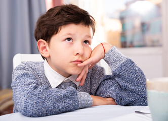 Wall Mural - Upset preteen boy sitting at table and thinks about problems