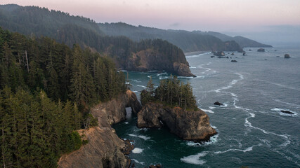 Aerial view of the coast of Oregon during sunset. The ocean can be seen with an arch at the Samuel H. Boardman Scenic Corridor.