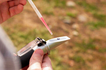 Wall Mural - the winemaker applies a drop of grape juice with a pipette to the prism of a refractometer to determine the amount of sugar in the grape juice