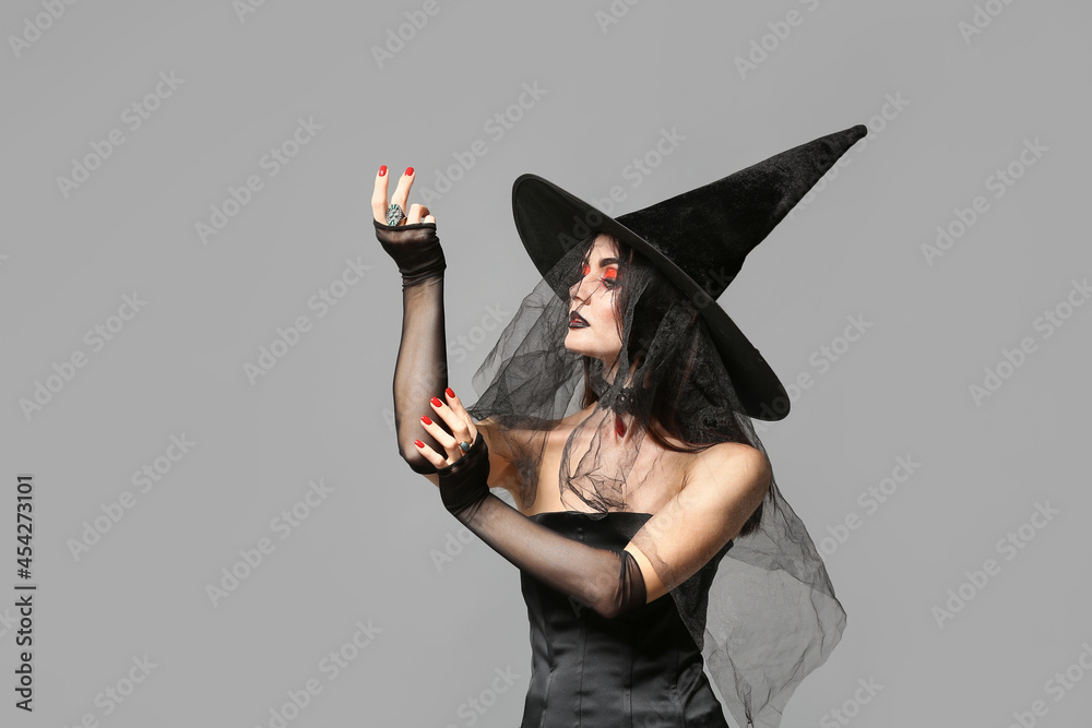Beautiful woman dressed as witch for Halloween on grey background