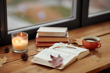 Wall Mural - season, leisure and objects concept - open book, cup of coffee, autumn leaves and candle on window sill at home