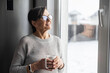 © Vadim Pastuh - Close-up portrait of senior older woman wearing glasses enjoys morning coffee in the kitchen at home. A modern retirement lady daydreaming with a mug of hot drink looks through the window