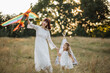 © sofiko14 - Happy native american family, mother and child daughter launch a kite on nature at sunset. Attractive woman shows her little child girl how to play with a kite in the field