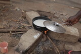 Fototapeta Most - horizontal photography of a black metal pot with rice boiling inside, standing on three concrete bricks over burning wood fire, outdoors in the Gambia, Africa